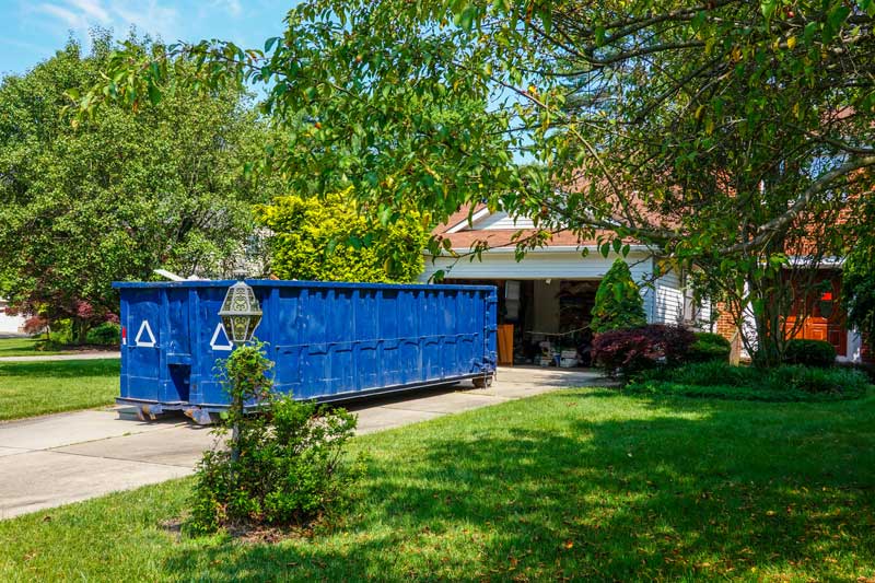 Blue dumpster sitting in a house's driveway
